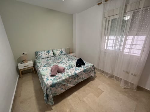 Acogedora habitación en apartamento de Fuengirola con cama floral, muebles blancos y vistas al frente de playa