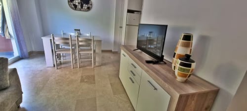 Sala de estar moderna en Fuengirola con mesa de comedor, televisor de pantalla plana y encimera de cocina con cestas decorativas