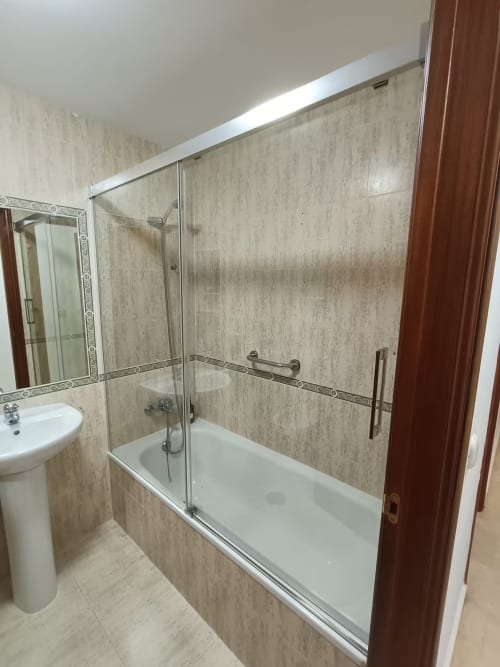Baño moderno con mamparas de ducha de cristal, paredes de azulejo beis y lavamanos pedestal en apartamento de Fuengirola