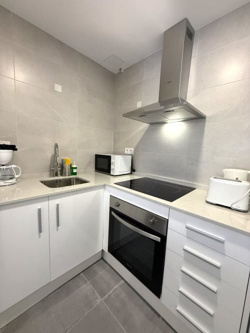 Cocina moderna en apartamento luminoso junto al mar, Fuengirola. Muebles blancos, campana extractora de acero inoxidable, placa de inducción.
