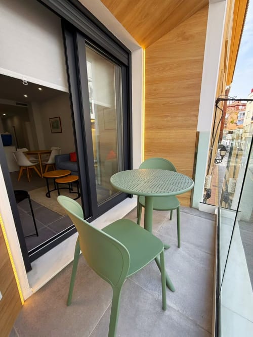 Balcón moderno de apartamento con asientos verdes vistas a Fuengirola, techo de madera y puertas de cristal
