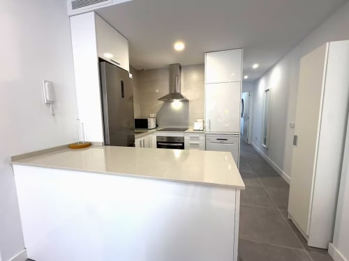 Cocina moderna con gabinetes blancos, encimeras beige y electrodomésticos de acero inoxidable en un luminoso apartamento nuevo