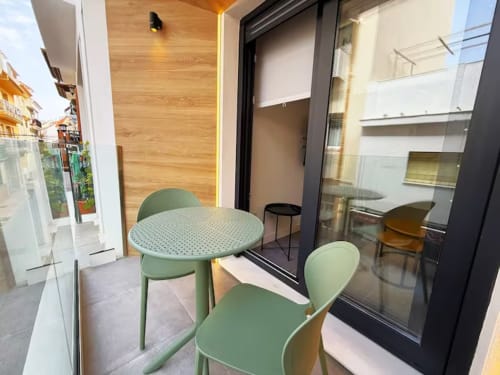 Balcón moderno de apartamento frente al mar en Fuengirola con sillas verdes, mesa redonda y vistas de la ciudad