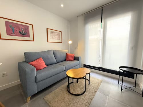 Moderno y luminoso salón con sofá gris, mesa de madera y amplias ventanas con vistas a la playa de Fuengirola
