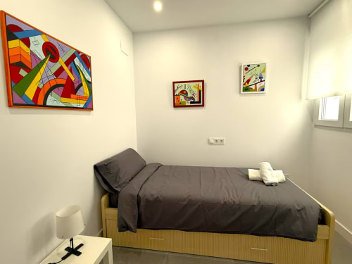 Dormitorio moderno en apartamento de Fuengirola con arte colorido, cama individual con ropa de cama oscura y luz natural abundante