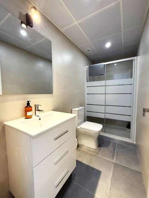 Baño moderno en apartamento de playa en Fuengirola con tocador blanco, inodoro y ducha con mampara de cristal