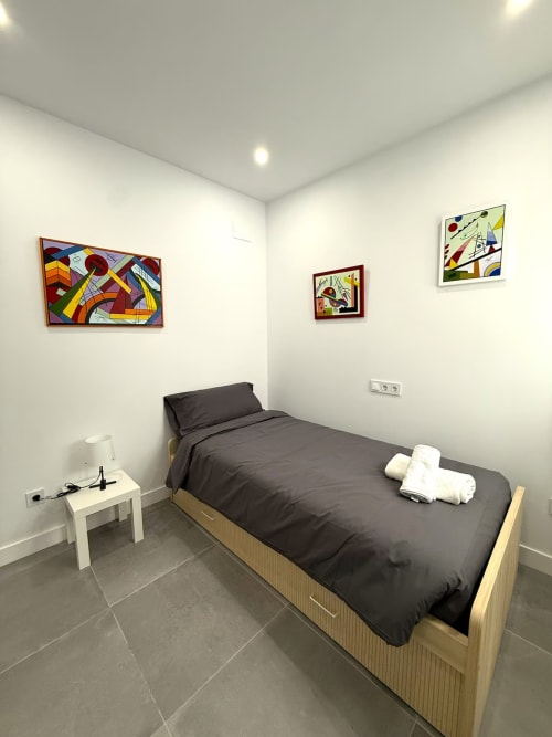 Moderno dormitorio en apartamento de playa en Fuengirola con cama, mesita de noche y obras de arte coloridas en paredes blancas