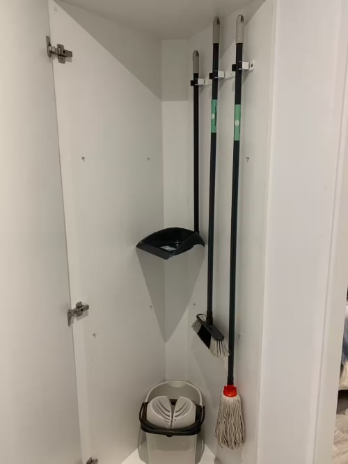 Armario de limpieza en apartamento de Fuengirola con productos de limpieza, cubo de basura y fregonas colgadas en ganchos