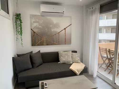 Moderno salón con sofá oscuro, plantas colgantes y cuadro de puente suspendido en apartamento de Fuengirola con vista al mar