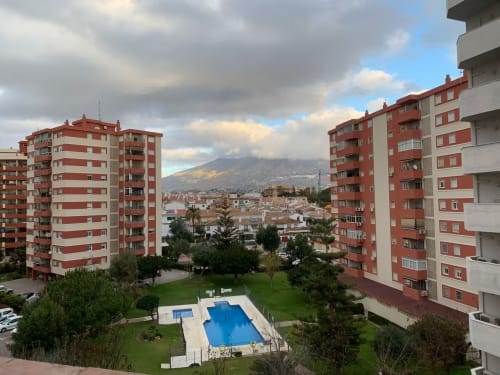 Edificios de apartamentos rojo y blanco con piscina compartida y patio verde con vistas a las montañas de Fuengirola