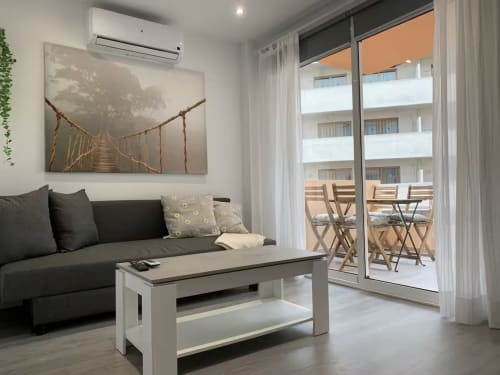 Moderno salón en Fuengirola con sofá oscuro, mesa de centro y balcón con vistas al mar