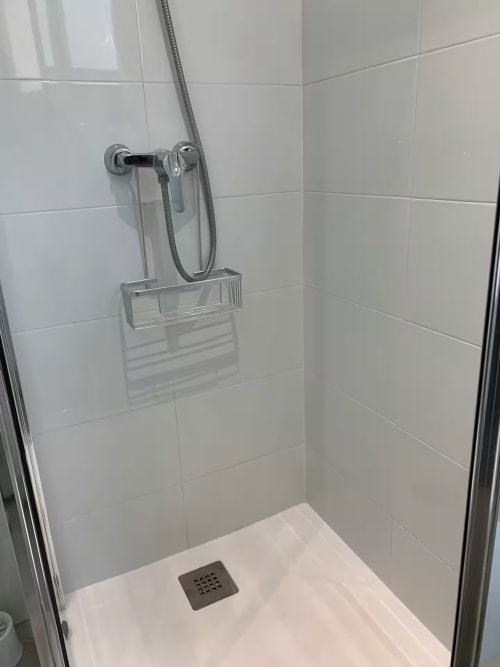 Moderno plato de ducha con azulejos blancos estilo metro, accesorios cromados y estante de cristal en baño de apartamento en Fuengirola
