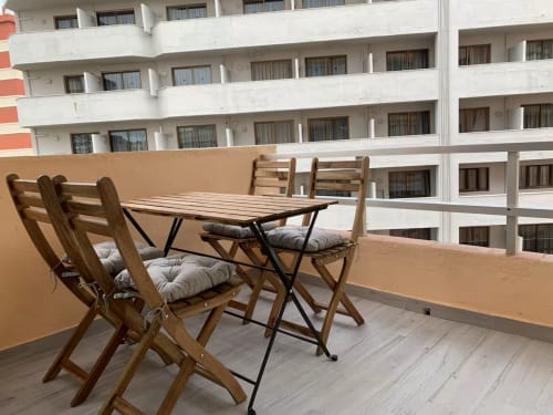Terraza amueblada en apartamento de Fuengirola con mesa de comedor de madera, sillas y vistas al mar del edificio blanco