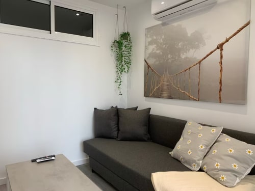 Moderno salón de apartamento en Fuengirola con sofá oscuro, plantas colgantes y cuadros de paisaje junto a la ventana
