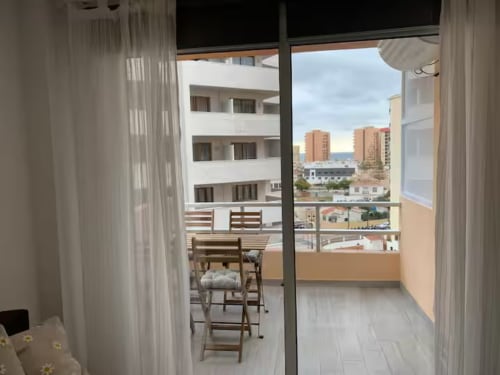 Vista de balcón del apartamento en Fuengirola con vistas al mar, sillas de madera y el perfil costero de fondo