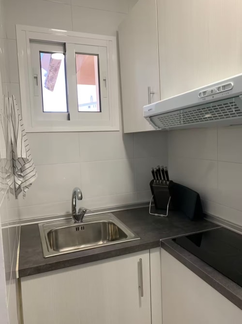 Cocina moderna en apartamento de Fuengirola con armarios blancos, encimera oscura, fregadero de acero inoxidable, placa de cocción y campana extractora