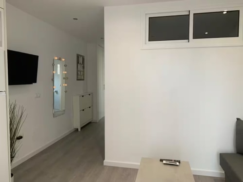 Sala de estar moderna en Fuengirola con televisor montado en la pared, espejo iluminado y mobiliario contemporáneo