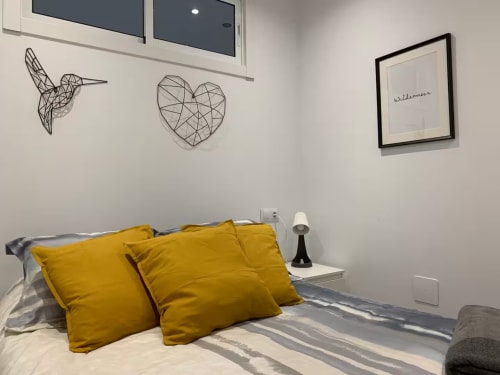 Dormitorio luminoso con almohadas amarillas, arte de pared de alambre y letrero de bienvenida enmarcado en apartamento de Fuengirola