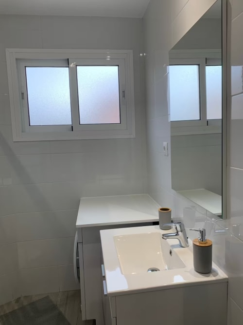 Baño moderno en apartamento de Fuengirola con lavamanos blanco, ducha con cristal esmerilado y ventana con vistas al mar