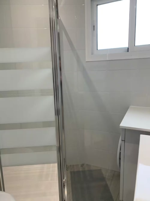 Baño moderno con cabina de ducha de cristal esmerilado, azulejos blancos y ventana en apartamento de Fuengirola