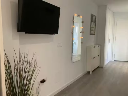 Pasillo moderno de apartamento con TV mural, espejo iluminado, muebles blancos y planta decorativa en hotel de Fuengirola