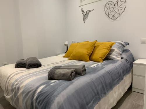 Acogedor dormitorio en apartamento de Fuengirola con ropa de cama a rayas, almohadas amarillas, toallas enrolladas y decoración minimalista en las paredes.