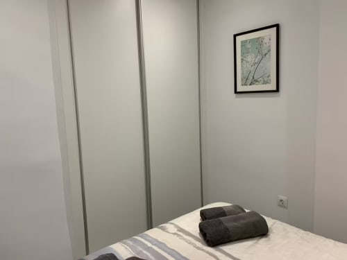 Dormitorio moderno en apartamento de Fuengirola con vista al mar, paredes blancas, armario deslizante y arte botánico enmarcado.