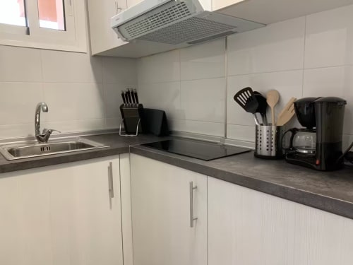 Cocina moderna con muebles blancos, encimera oscura, fregadero de acero inoxidable, vitrocerámica y electrodomésticos en apartamento de Fuengirola
