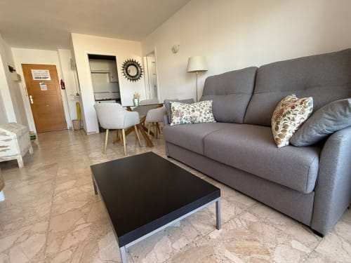 Sala moderna con sofá gris, mesa de centro negra y zona de comedor en apartamento de playa en Fuengirola de Grupo Inmo House