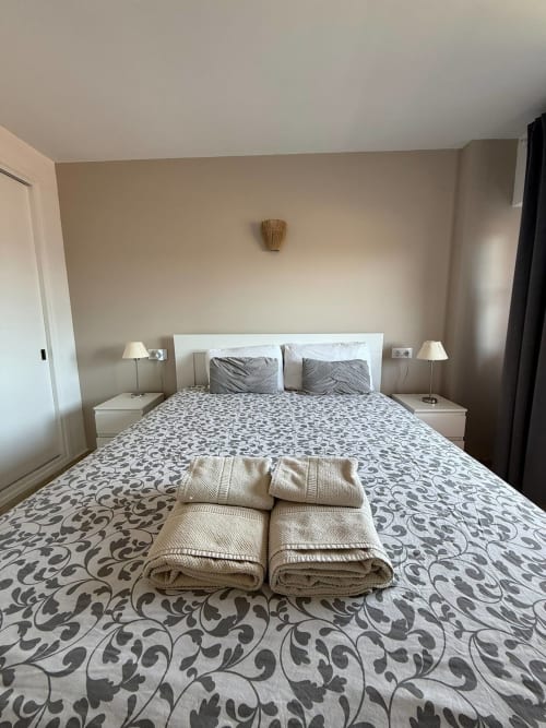 Dormitorio moderno en apartamento de Fuengirola con ropa de cama estampada, cabecero blanco y toallas enrolladas acogedoras