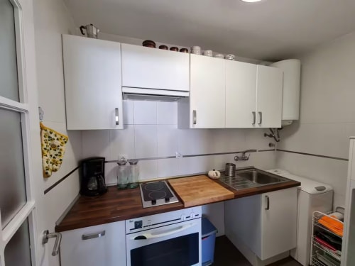 Cocina compacta moderna en apartamento de Fuengirola con muebles blancos, encimera de madera y electrodomésticos de acero inoxidable