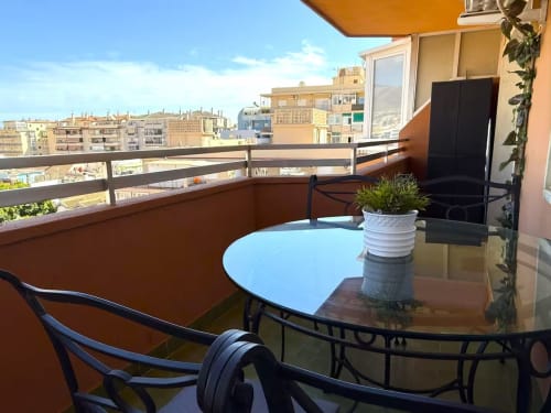 Balcón luminoso con vistas a edificios de Fuengirola, apartamento amueblado con mesa, sillas y vistas a la montaña