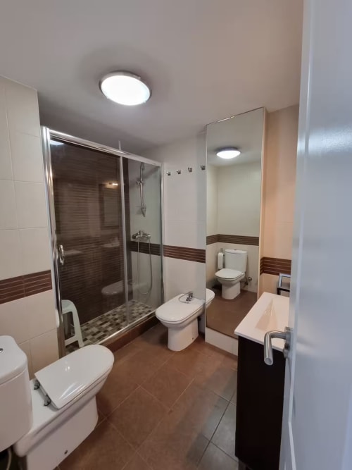 Baño moderno en apartamento de Fuengirola con mampara de ducha de cristal, doble lavabo y detalles en azulejos marrón
