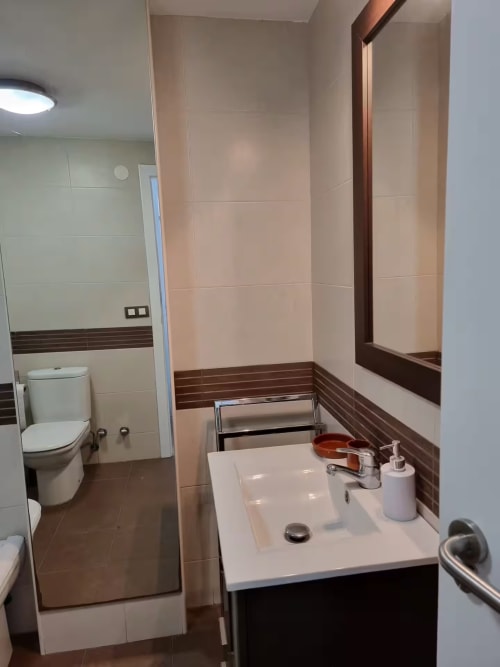Baño moderno en apartamento de Fuengirola con lavabo blanco, detalles en azulejos marrones, inodoro y espejo