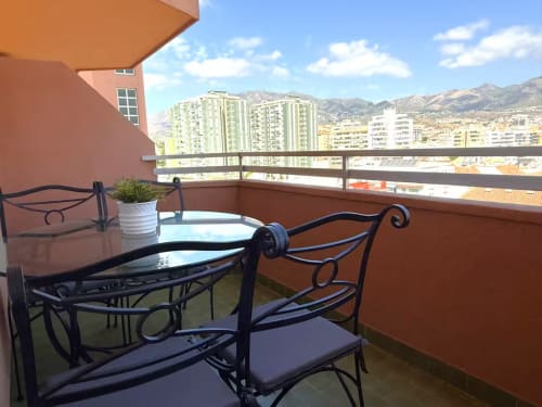 Balcón amueblado con asientos de hierro forjado con vistas a las montañas de Fuengirola y apartamentos, con zona de comedor al aire libre