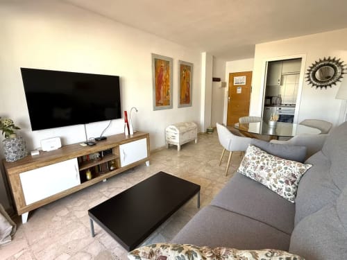 Moderno salón en apartamento de Fuengirola con sofá gris, televisor, mueble de entretenimiento en madera y acceso a cocina