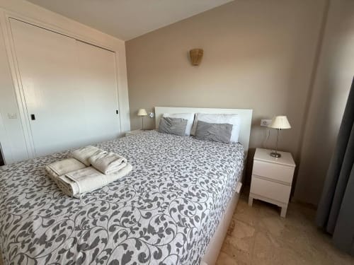 Dormitorio luminoso en apartamento de Fuengirola con ropa de cama estampada, mesillas blancas con lámparas y puertas de armario deslizantes
