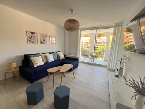 Luminoso apartamento de playa en Fuengirola con sofá azul marino, mesas de madera y vistas al jardín de la terraza
