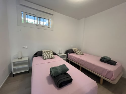 Habitación doble con ropa de cama rosa en apartamento frente al mar Grupo Inmo House en Fuengirola, con luz natural desde la ventana