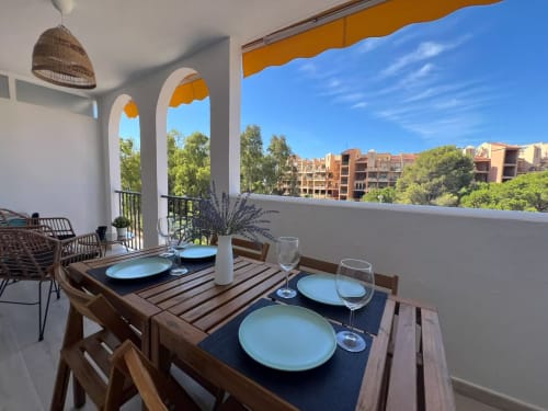 Balcón de apartamento frente al mar en Fuengirola con mesa de comedor, platos azules, arcos y vistas al jardín costero bajo cielo despejado