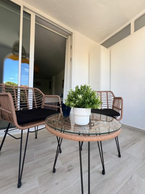 Zona de descanso en terraza moderna con sillas tejidas, mesa de cristal y maceta en apartamento frente al mar en Fuengirola