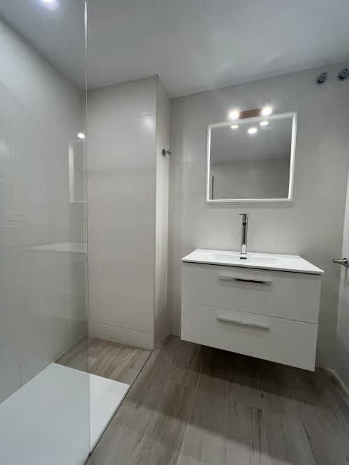 Baño moderno con tocador blanco, espejo iluminado y cabina de ducha de cristal en apartamento frente al mar de Fuengirola