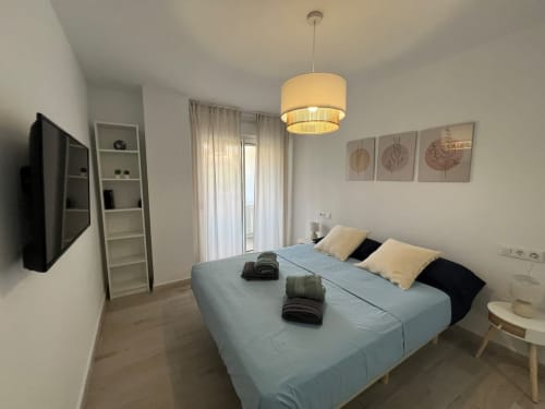 Moderno dormitorio en apartamento de playa en Fuengirola con cama queen, TV, lámpara colgante y acceso a balcón