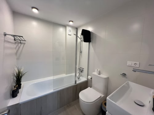 Baño moderno en apartamento de playa en Fuengirola con bañera, ducha, inodoro, lavabo y azulejos blancos