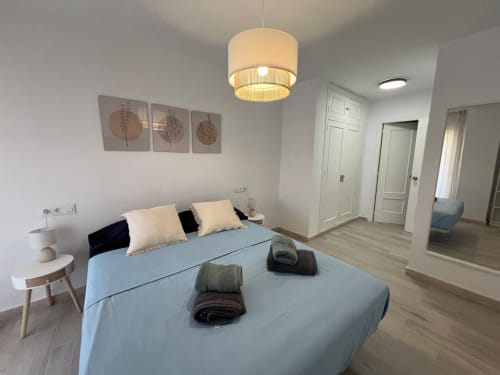Dormitorio moderno de apartamento en Fuengirola con cama azul, luz colgante, arte botánico y puerta de baño privado