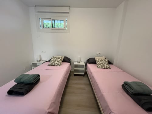 Dormitorio doble con ropa de cama rosa en apartamento de playa en Fuengirola, mesilla blanca, almohadas estampadas, ventana con vistas al jardín