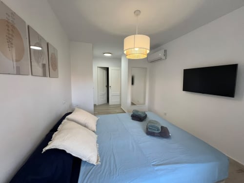 Moderno dormitorio en apartamento de playa en Fuengirola con cama, TV, lámpara colgante y mobiliario contemporáneo