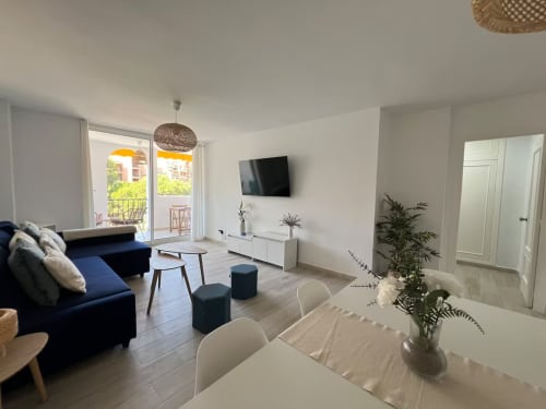 Luminoso apartamento moderno en Fuengirola con sofá azul marino, zona de comedor, TV, balcón y vistas al jardín