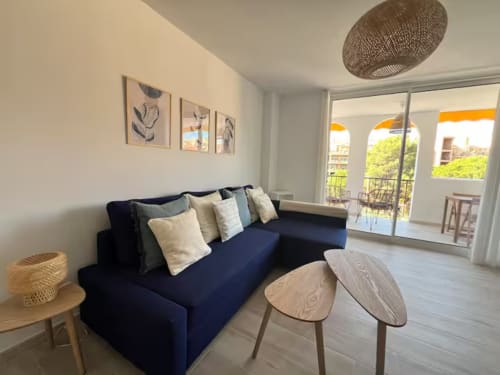 Sala de estar de apartamento moderno en Fuengirola con sofá azul marino, mesitas de madera y acceso a terraza con vistas al jardín