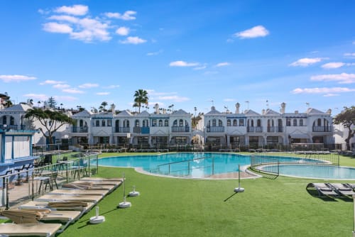 Piscina color turquesa con tumbonas, jardín verde exuberante y apartamentos de estilo mediterráneo blanco en Home Stay Gran